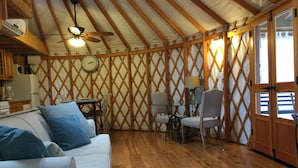 A cozy room with a wooden ceiling, a dining table with chairs, a white sofa, and a clock on the wall.
