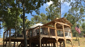 A wooden treehouse with a balcony, surrounded by trees and a clear sky.