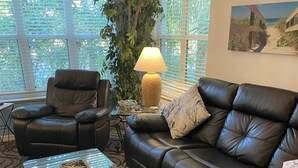 Een woonkamer met een leren bank, een lederen fauteuil, een glazen salontafel en een lamp.