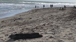 Een zandstrand met mensen die wandelen en spelen, en de oceaan op de achtergrond.
