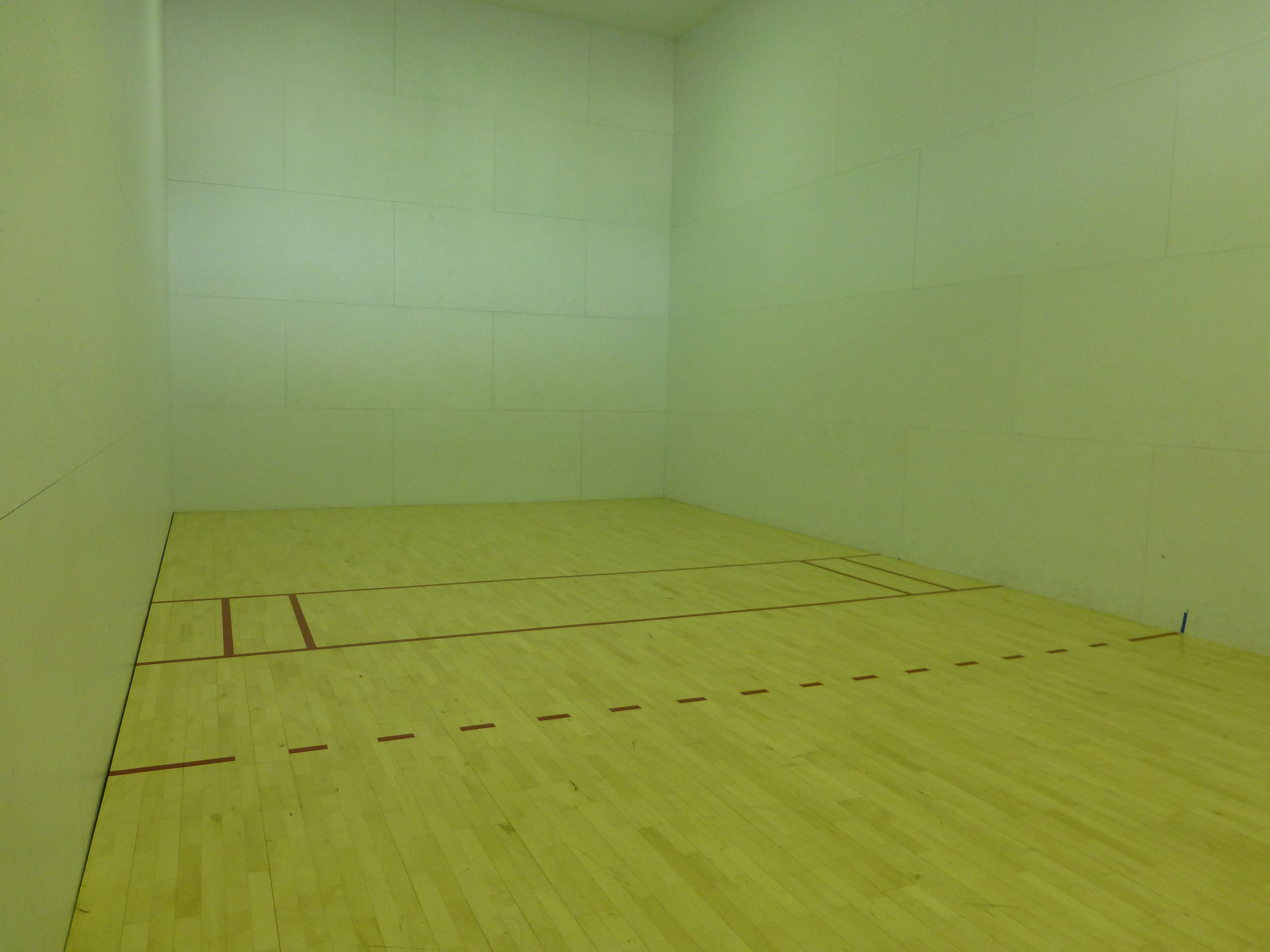 Una cancha de squash con piso de madera y paredes blancas.