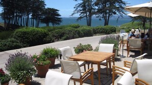 An outdoor patio with wooden tables and white chairs, surrounded by potted plants and overlooking a scenic view of the ocean. - Seascape Resort 2B Luxury Oceanview Villa, Steps From The Beach, 5 min to golf (Aptos)
