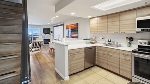 A modern kitchen with wooden cabinets, a white countertop, stainless steel appliances, and a dining area with a bar. - Seascape Resort 2B Luxury Oceanview Villa, Steps From The Beach, 5 min to golf (Aptos)
