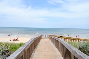 A wooden boardwalk leading to a beach with people and umbrellas. - Luxury Beach Condo at Cinnamon Beach (Palm Coast)