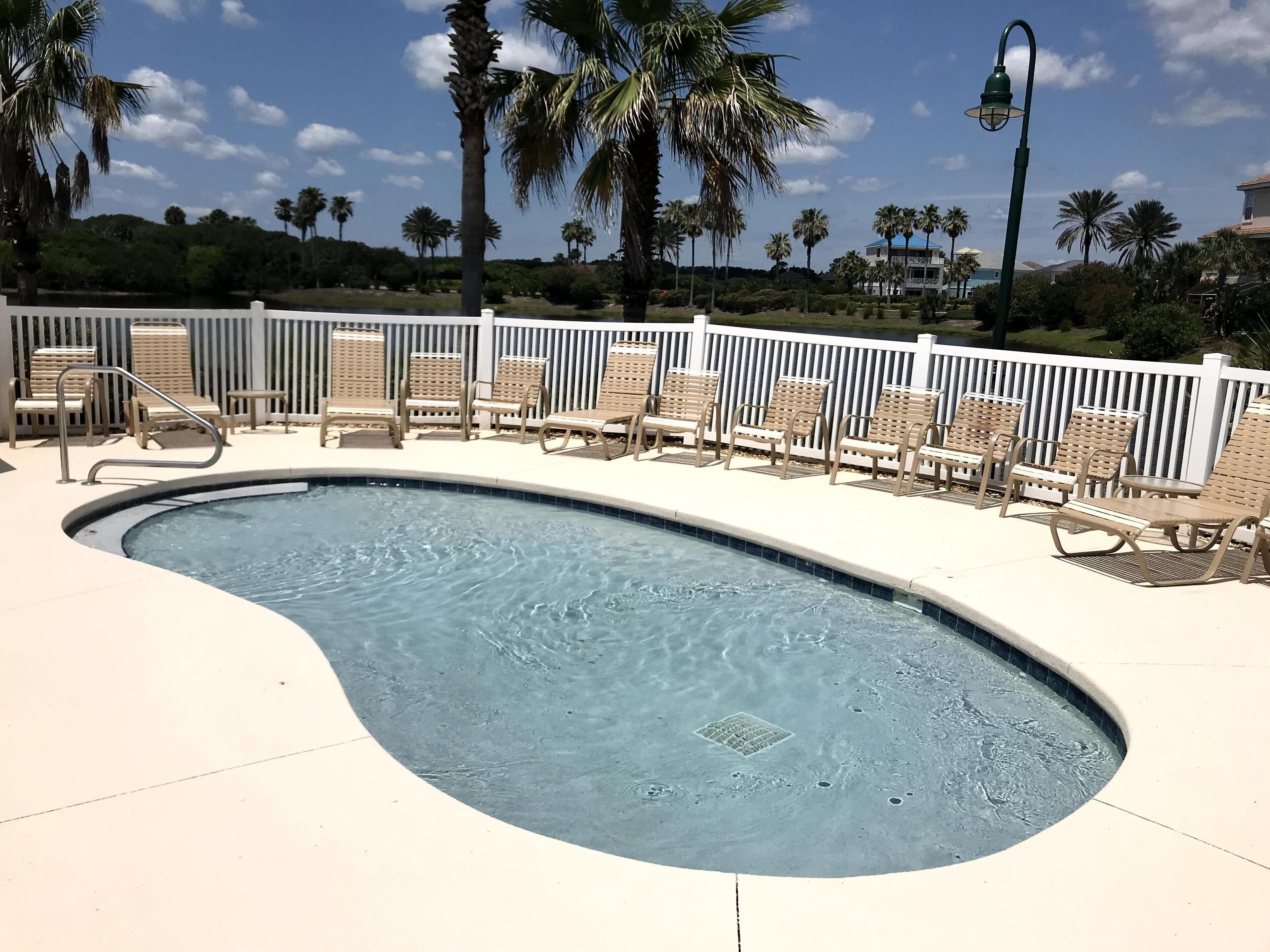A swimming pool with lounge chairs and a white fence.