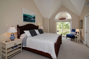 Une chambre à coucher avec un grand lit, deux tables de chevet, une commode, une fenêtre avec vue et un ventilateur de plafond.