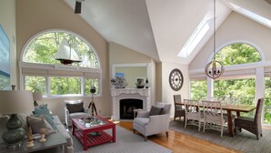 A spacious living room with a fireplace, large windows, and a dining area with a chandelier.