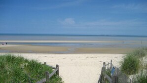 A beach with a wooden walkway leading to the water, a sandy shore, and a clear sky.