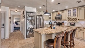 A modern kitchen with stainless steel appliances, a granite countertop island, and a seating area with leather chairs. - Lake Conroe WATERFRONT Updated 3BR Condo with Pools, Paddle Boards & Views (Montgomery)
