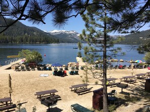 Una playa junto al lago con mesas y sillas de picnic, una parrilla de barbacoa y vistas a una cadena montañosa.