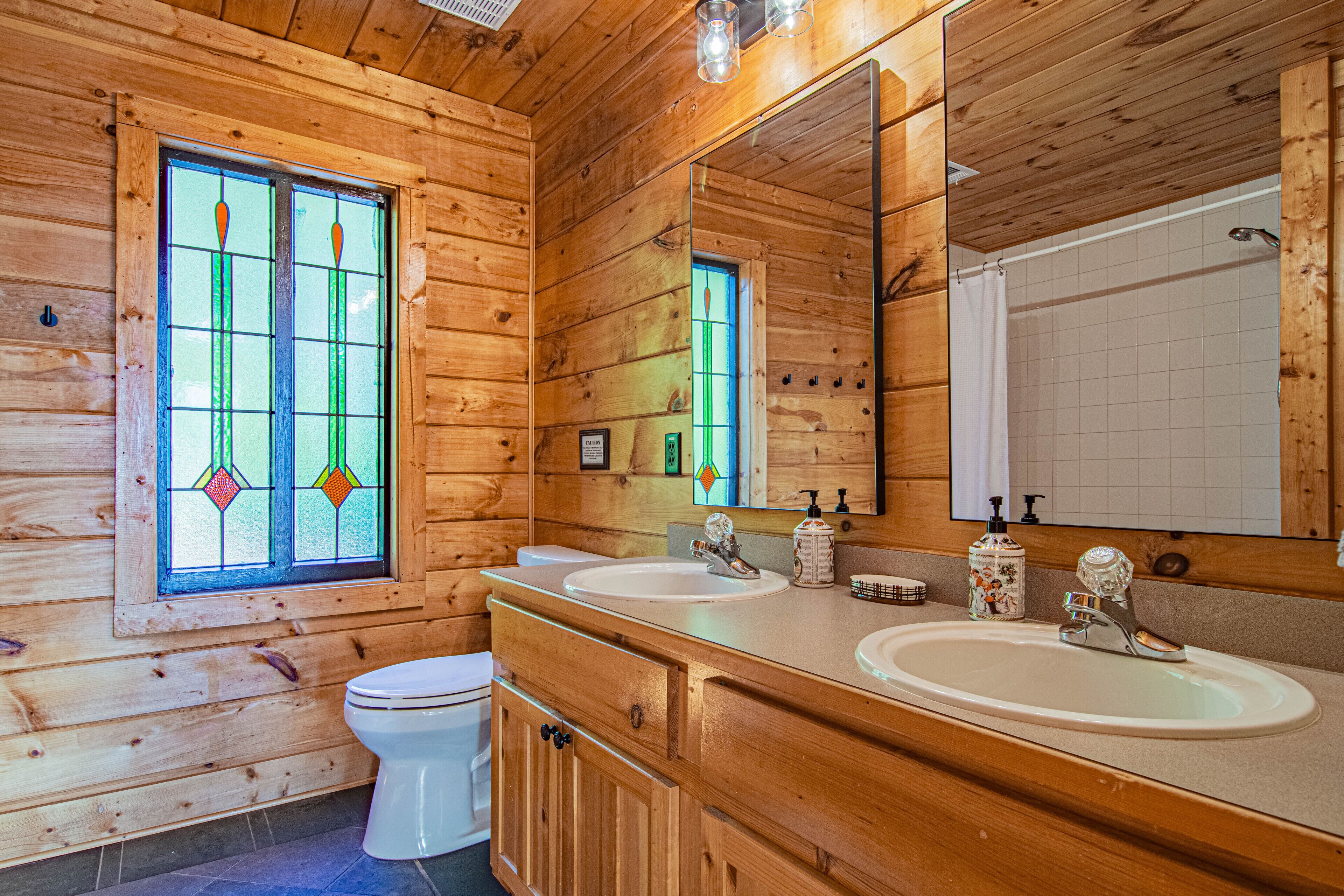 Un baño de cabaña de madera con dos lavamanos, un inodoro y un espejo grande.