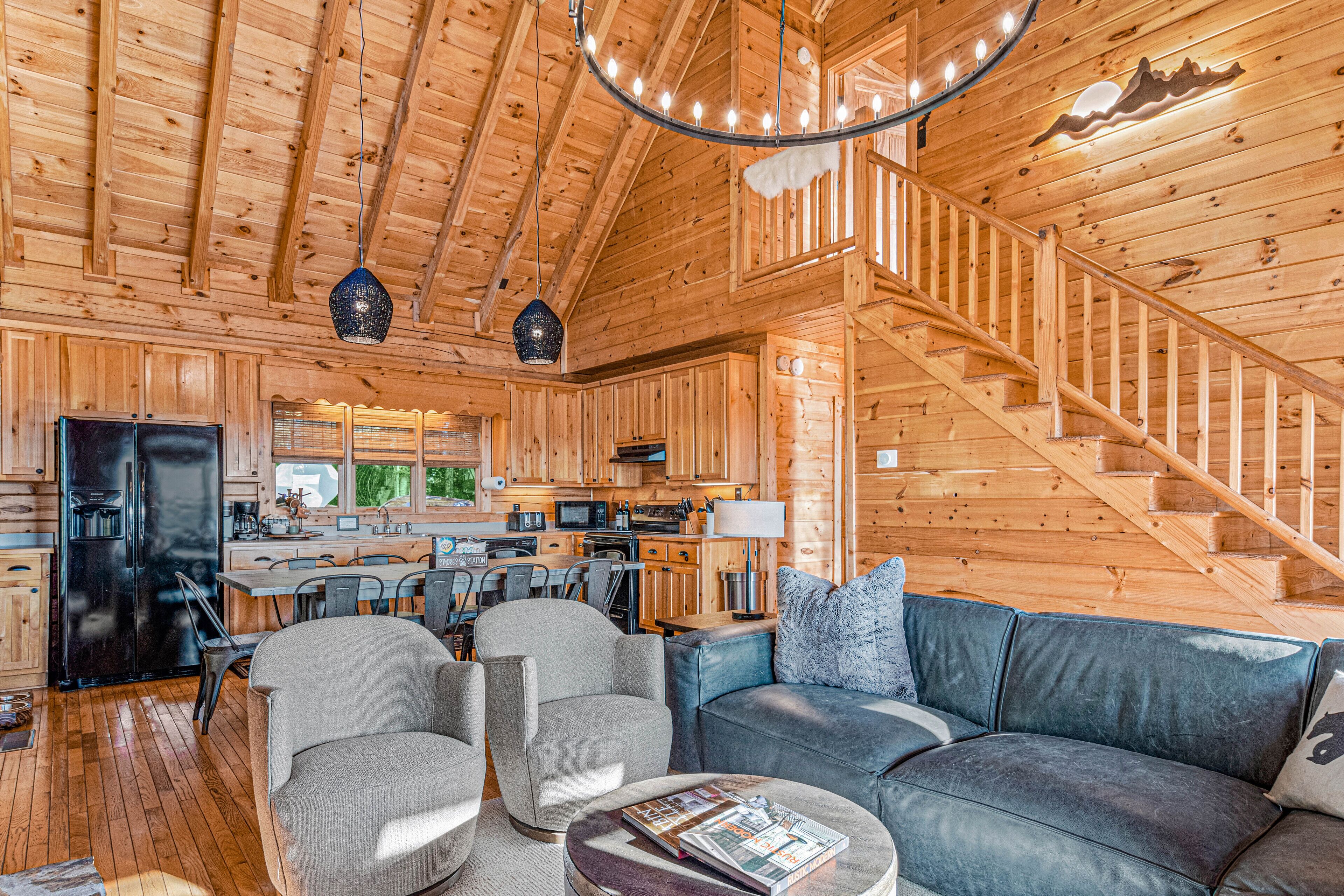 Interior de una cabaña de madera con comedor, cocina y una escalera.