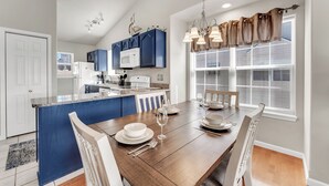 Une cuisine moderne avec des meubles bleus, un îlot central et un coin repas doté d’une table en bois, mise pour quatre personnes.