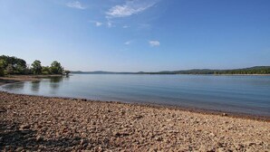 Un lac paisible, avec une rive de galets et des collines qui se dessinent à l’horizon.