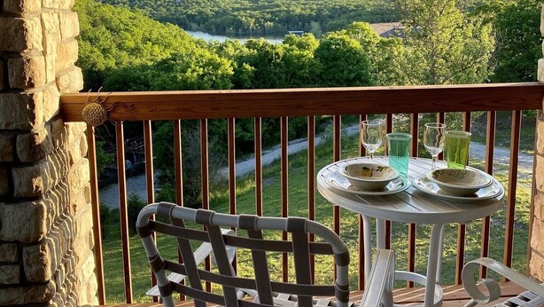 Une terrasse en bois avec une arche en pierre, une chaise en métal et une petite table ronde avec des assiettes et des verres.