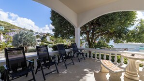 An outdoor patio with chairs and a table, surrounded by a white balustrade, overlooking a hillside with buildings and trees. - Gated "Sea Breeze" House Overlooking the Caribbean (Patillas)