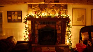A cozy living room with a stone fireplace, decorated with Christmas lights and a garland. There is a framed picture on the wall and a basket on the floor.
