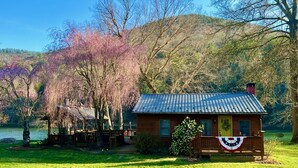 A cabin with a porch, surrounded by lush greenery and a lake.