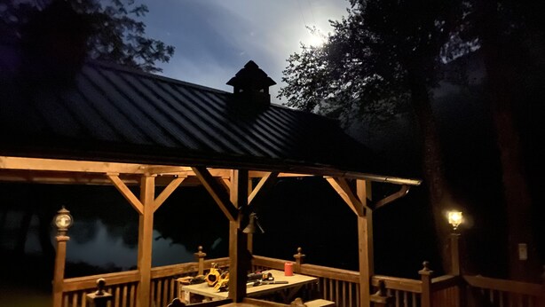 A wooden gazebo with a metal roof overlooking a body of water.