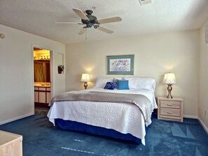 A bedroom with a bed, two bedside tables with lamps, a ceiling fan, a framed floral artwork, and a bathroom visible through an open door. - By Strip~Walk-In~Clean~2 Kings~Indoor Pool~HotTub (Branson)