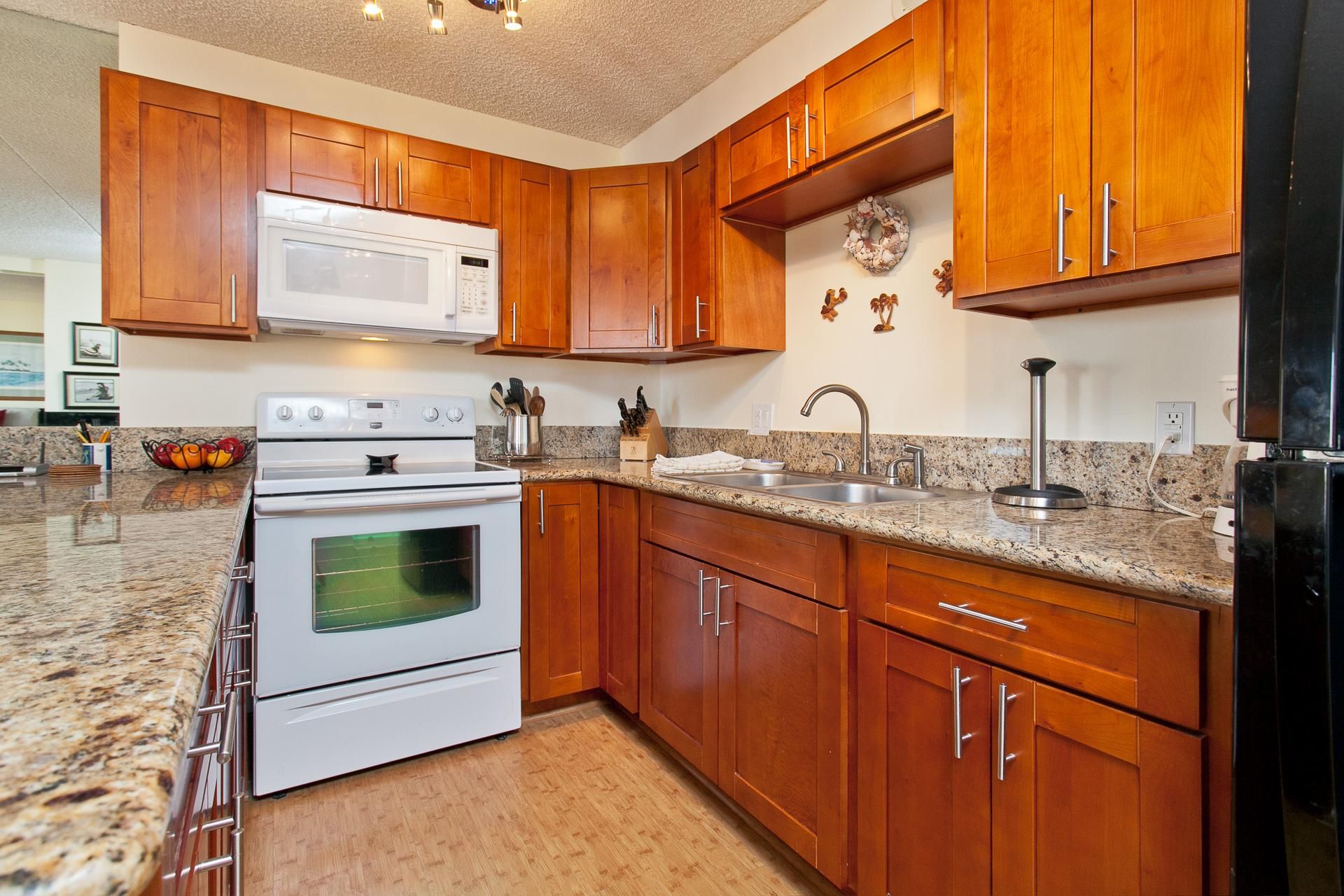 Kitchen with granite countertops, warm wood cabinets, white electric stove, and built-in microwave above.
