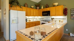 A kitchen with wooden cabinets, a white refrigerator, a microwave, and a large island with jars.