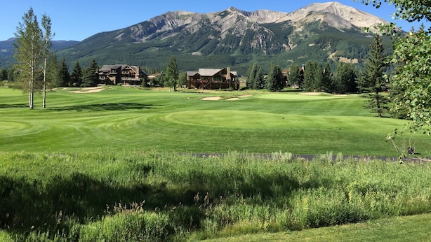A golf course with a mountain backdrop, surrounded by lodge buildings.