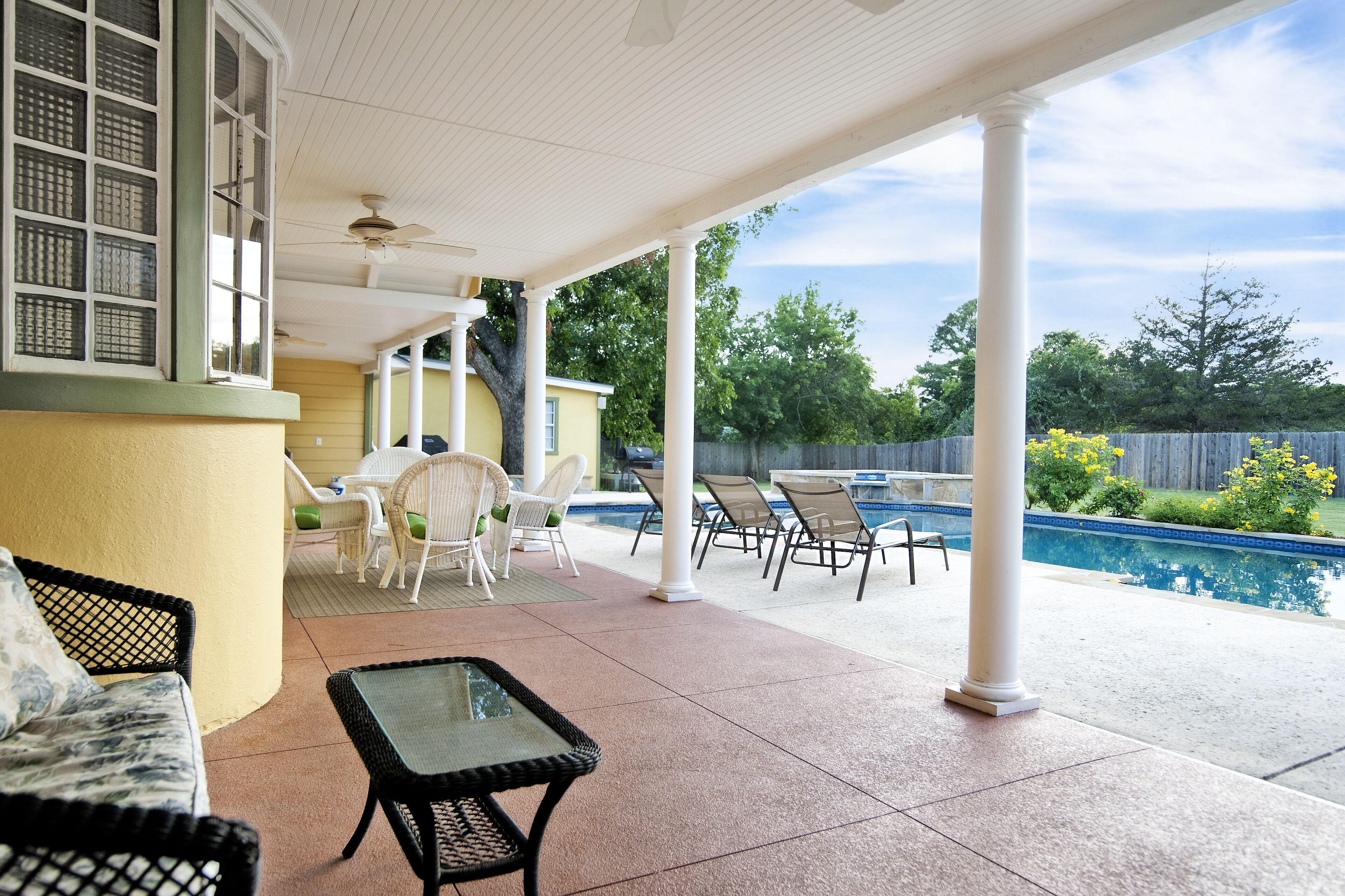 Un patio couvert avec une piscine, du mobilier d’extérieur et une vue sur la végétation environnante.
