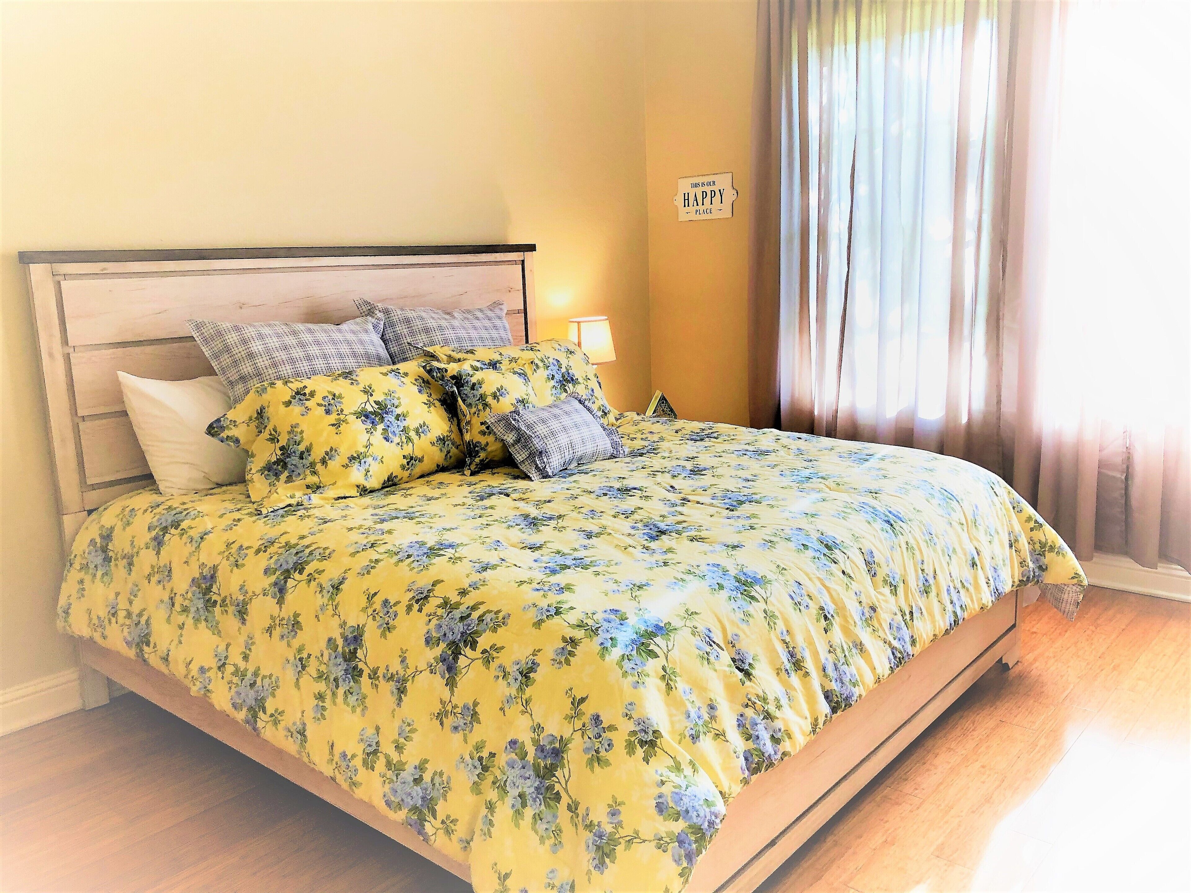 A bed with floral bedding, a wooden headboard, and a sign on the wall.