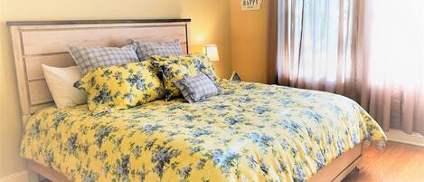 A bed with floral bedding, a wooden headboard, and a sign on the wall.