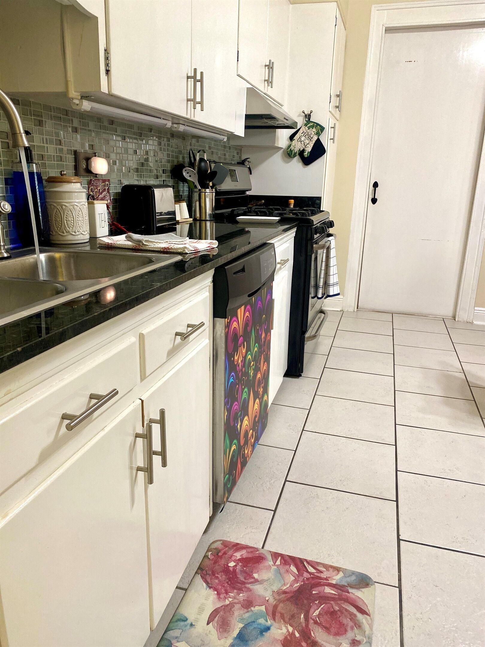 A kitchen with white cabinets, a black countertop, and a colorful floral rug.