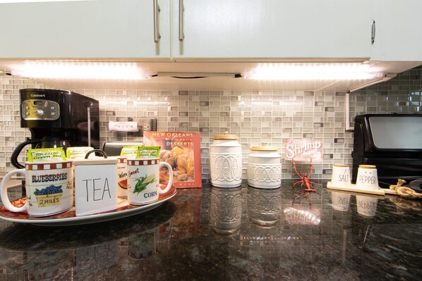 A kitchen counter with a coffee maker, tea and coffee mugs, a book, salt and pepper shakers, and a decorative spider.