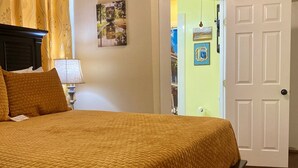 A bedroom with a large bed, a nightstand, a lamp, and a door leading to another room.
