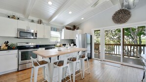 Une cuisine moderne avec des meubles blancs, des appareils en acier inoxydable et une table à manger en bois, accompagnée de tabourets de bar.
