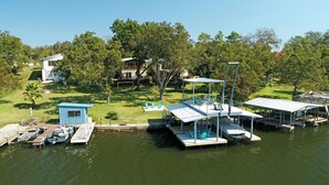 Une propriété au bord du lac, dotée d’un quai, d’un petit bâtiment bleu et d’une grande terrasse avec des chaises et des tables.
