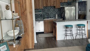 A modern kitchen with wooden cabinets, a stainless steel refrigerator, and a bar area with stools.