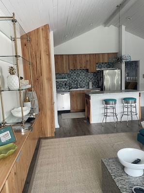 A modern kitchen with wooden cabinets, a stainless steel refrigerator, and a bar area with stools.