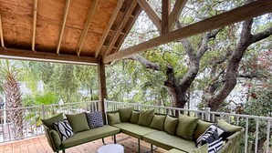 A covered outdoor seating area with a green wicker sofa and a white table.
