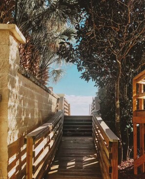 Eine Holztreppe führt zu einem Strand, umgeben von Palmen und einem klaren Himmel.