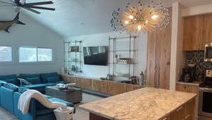 A modern living room with a blue sofa, a coffee table, and a kitchen area with wooden cabinets and a marble countertop.