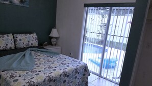 Une chambre à coucher comprenant un lit, une table de chevet, une lampe et une vue sur une piscine, accessible par une porte coulissante.