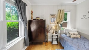 A bedroom with a bed, a nightstand, a dresser, a window with curtains, and a wall with a framed picture.