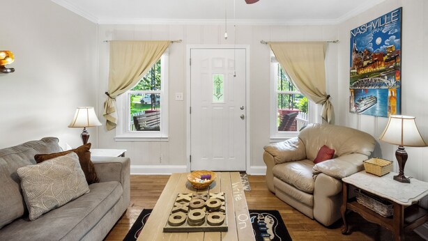 A living room with a beige sofa, a leather armchair, a coffee table with wooden blocks, and a ceiling fan.