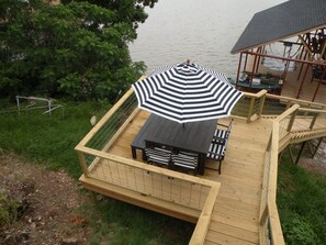 A wooden deck with a table and chairs, a striped umbrella, and a view of the water. - Private, Lake-Front, Guest Suite on Lake Granbury, near downtown! (Granbury)