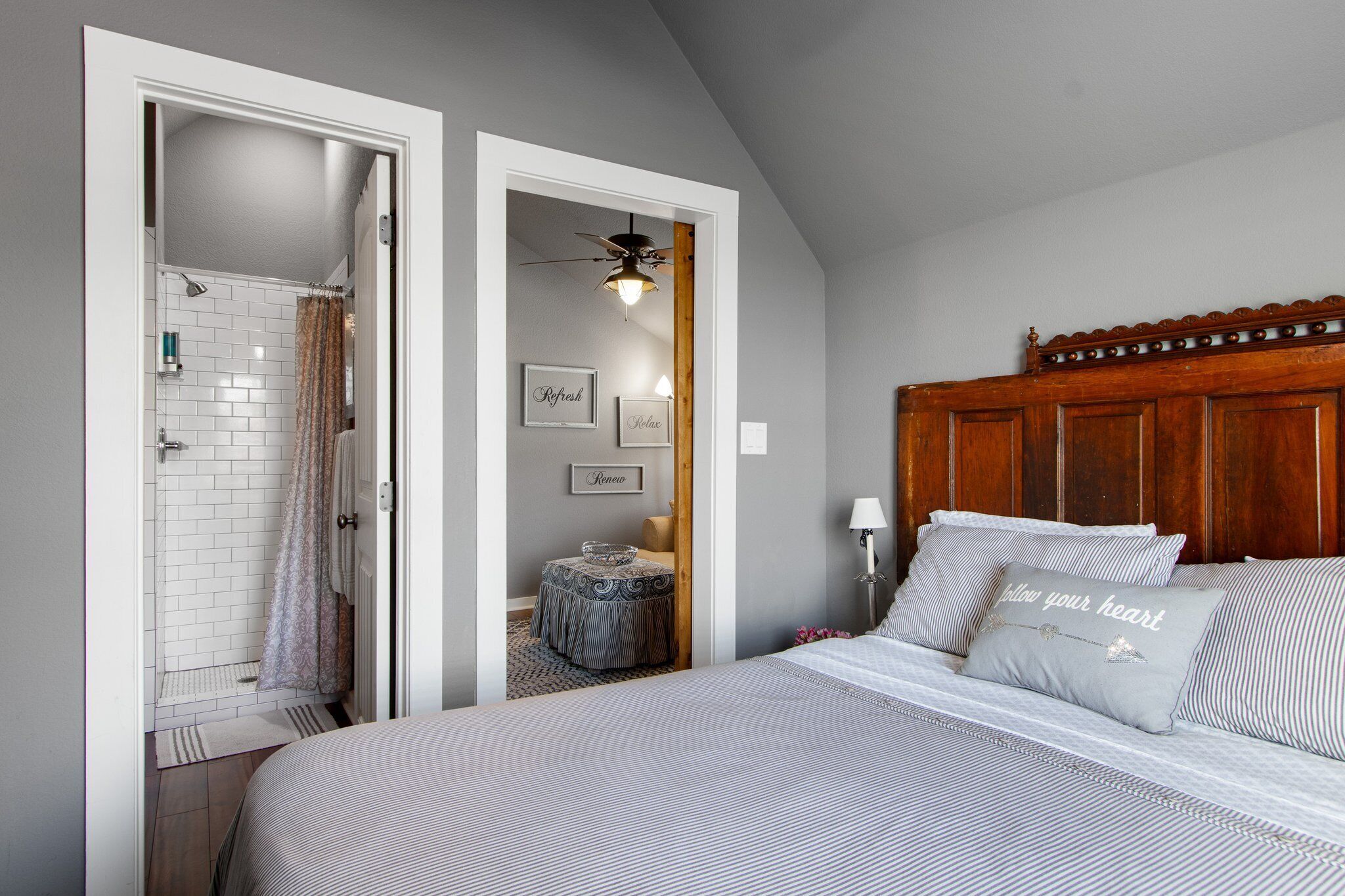 A bedroom with a large bed, a wooden headboard, a small bedside table, and a shower area visible through an open door.