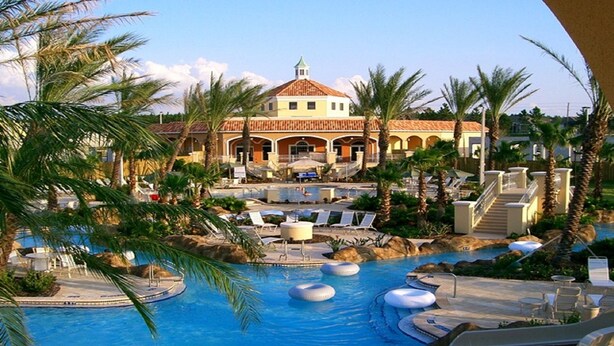Un resort con una gran piscina, palmeras y un edificio con techo de tejas.