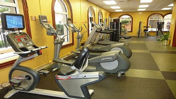 Un gimnasio con varias máquinas de cardio, incluyendo cintas de correr y elípticas, dispuestas en fila.
