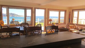 A dining area with a view of the ocean, featuring a table and chairs, a laptop on the table, and a balcony with a railing. - MENDO VILLAGE LUXURY OCEANFRONT PENTHOUSE, DOG FRIENDLY, VIEWS, WALK EVERYWHERE! (Mendocino)