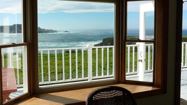 A room with a large window overlooking a coastal view, featuring a wooden deck and a white railing. - MENDO VILLAGE LUXURY OCEANFRONT PENTHOUSE, DOG FRIENDLY, VIEWS, WALK EVERYWHERE! (Mendocino)