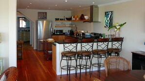 A kitchen with a central island, bar stools, and a dining area with wicker chairs. - MENDO VILLAGE LUXURY OCEANFRONT PENTHOUSE, DOG FRIENDLY, VIEWS, WALK EVERYWHERE! (Mendocino)